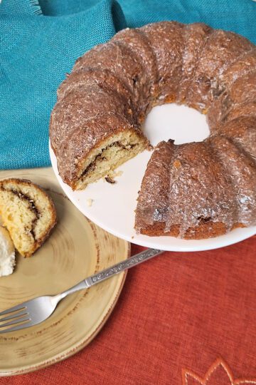 sour cream coffee cake on a white cake stand with a brown plate with cake and ice cream and fork