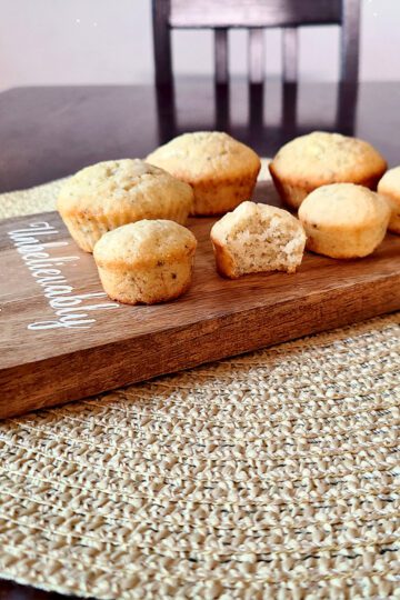 banana bread muffins on a wooden cutting board on a tan mat on a dark table