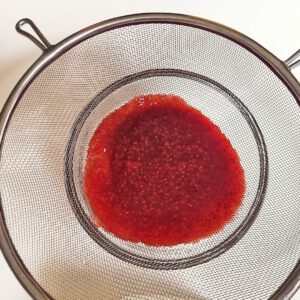 Metal sieve over saucepan to strain raspberry seeds from sauce