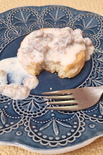 Sausage gravy over biscuit on a blue plate