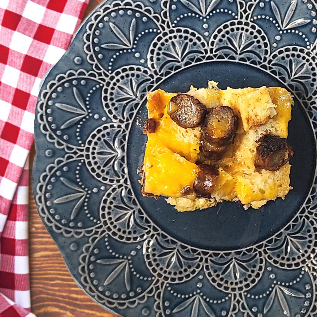 Christmas breakfast casserole on a blue plate with a red and white checkered cloth napkin on the side
