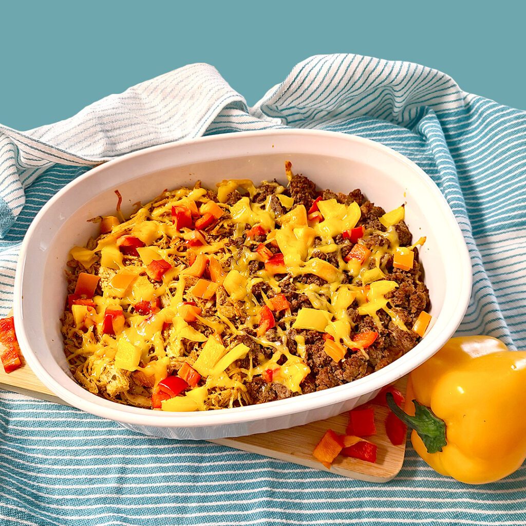 Leftovers taco bake in an white oval dish with teal dish cloth and bell peppers around