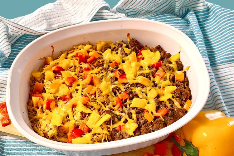 Leftovers taco bake in an white oval dish with teal dish cloth and bell peppers around
