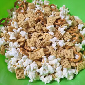 Popcorn, Chex cereal, peanuts, and pretzels in a large green bowl