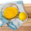 lemon curd in a glass bowl on a teal striped towel with a lemon on a wooden cutting board