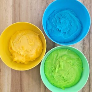 yellow, blue, and green buttercream frosting in coordinating colored bowls