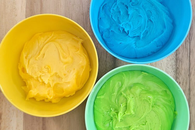 yellow, blue, and green buttercream frosting in coordinating colored bowls