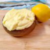 lemon buttercream frosting in a wooden bowl next to a lemon on a wood cutting board