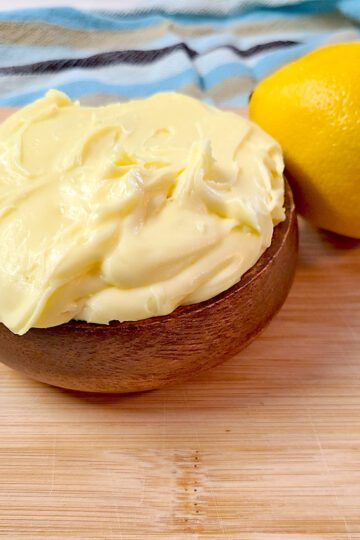lemon buttercream frosting in a wooden bowl next to a lemon on a wood cutting board