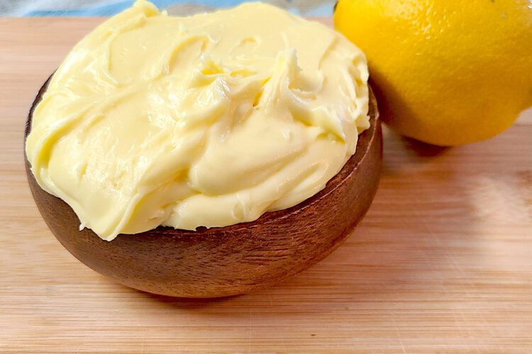 lemon buttercream frosting in a wooden bowl next to a lemon on a wood cutting board