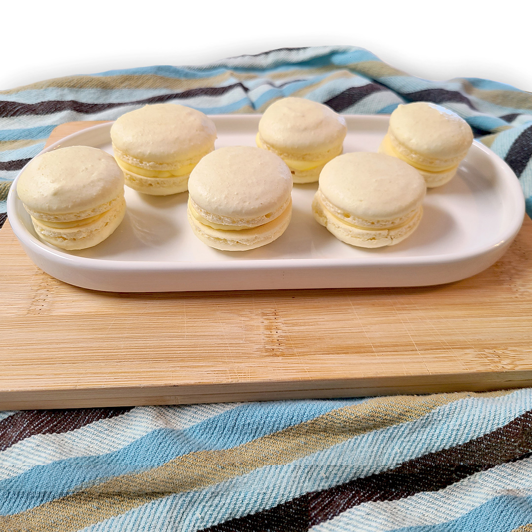 six lemon macaroons on a white oval dish on a wood cutting board with a striped towel underneath