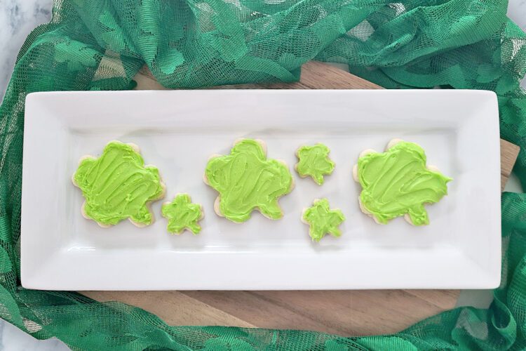 shamrock shaped gluten free sugar cookies with lime green frosting on a white rectangluar platter with green lace around it