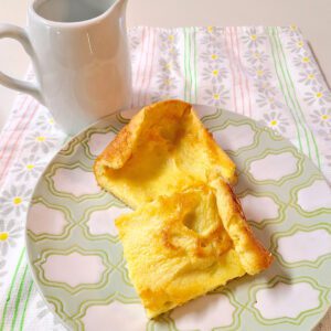 german pancakes on a green and white plate with a small white pitcher behind