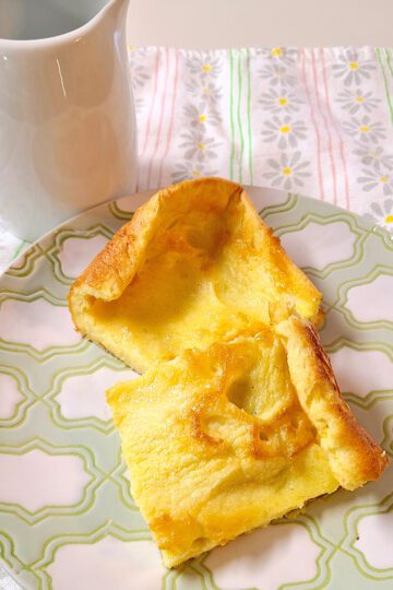 german pancakes on a green and white plate with a small white pitcher behind