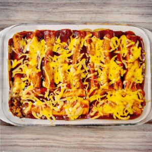 beef enchiladas cooked with cheese on top in a 9x13 glass pan with a wooden background