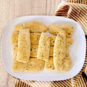 gluten free garlic breadsticks on white platter with a striped cloth under on a wooden board