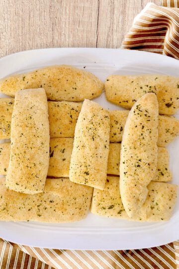gluten free garlic breadsticks on white platter with a striped cloth under on a wooden board
