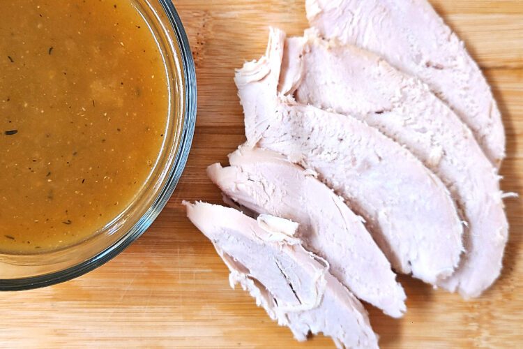 Herb roasted turkey slices next to a bowl of homemade gravy on a wooden cutting board