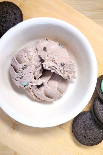 mint oreo ice cream in a white bowl surrounded by mint oreos on a wooden board