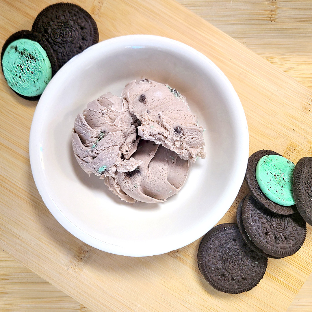 mint oreo ice cream in a white bowl surrounded by mint oreos on a wooden board