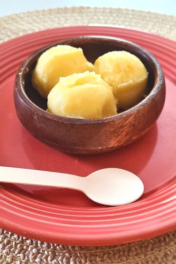 pineapple sorbet in a wood bowl on a medium pink plate on a tan placemat