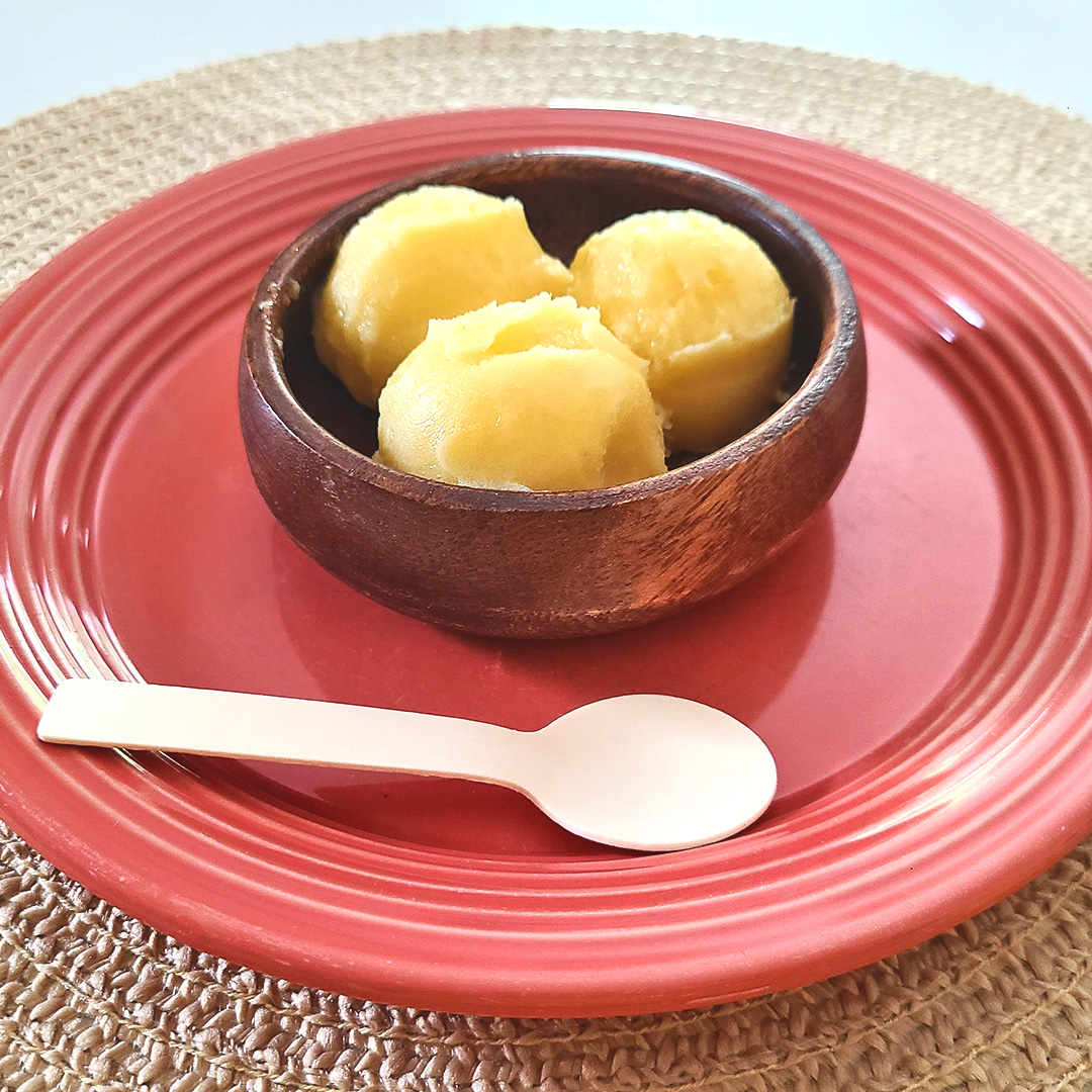 pineapple sorbet in a wood bowl on a medium pink plate on a tan placemat