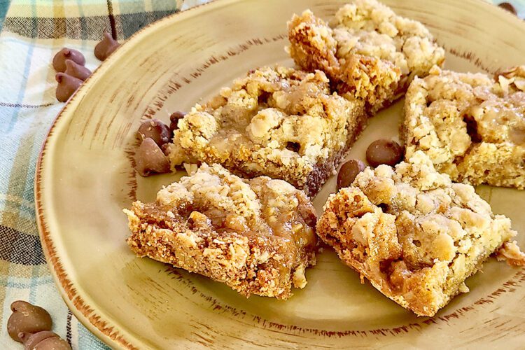 Carmelitas on a brown plate with a few chocolate chips sprinkled around, and a blue plaid towel underneath the plate