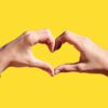 two hands making a heart with a yellow background