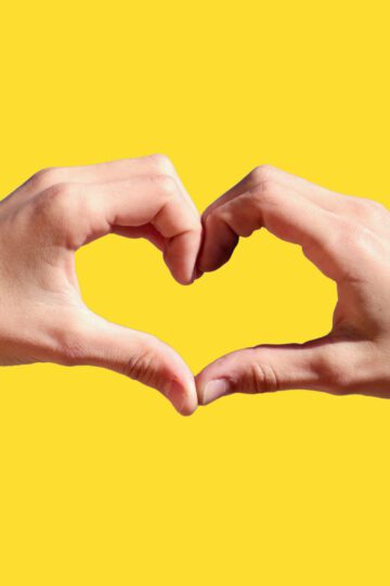 two hands making a heart with a yellow background