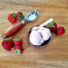 strawberry ice cream in a wooden bowl surrounded by fresh strawberries and a antique ice cream scoop all on a wooden board
