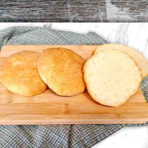 gluten free hamburger buns on a wood cutting board with a blue plaid cloth underneath on the countertop