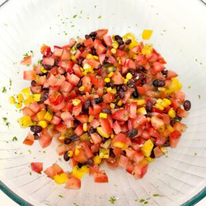 chopped tomatoes, bell peppers, black beans, and corn with cilantro-lime vinaigrette in a large glass bowl