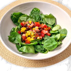 spinach salad in a white bowl on a light brown circular mat on a white and gray countertop