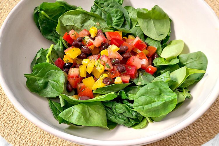 spinach salad in a white bowl on a light brown circular mat on a white and gray countertop