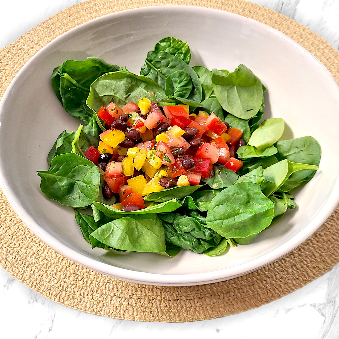 spinach salad in a white bowl on a light brown circular mat on a white and gray countertop