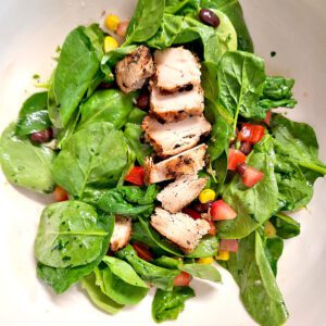 spinach salad with cilantro-lime vinaigrette with grilled chicken on top in a white salad bowl