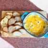 cheesy bacon dip in a oval blue dish with gluten free bread and crackers on a wooden cutting board