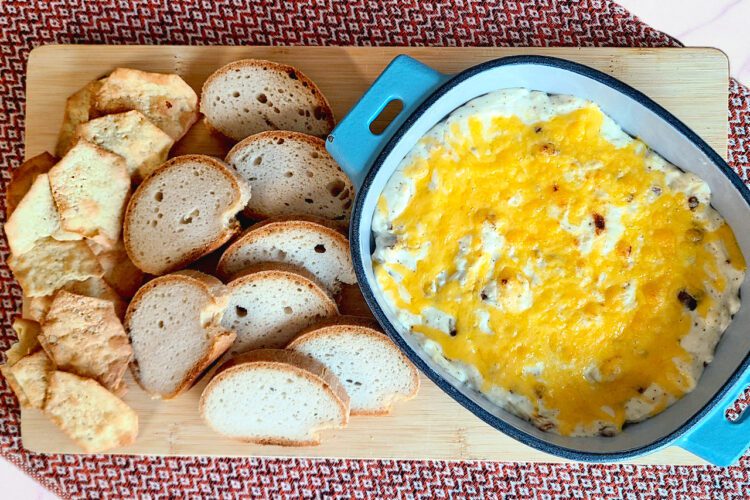 cheesy bacon dip in a oval blue dish with gluten free bread and crackers on a wooden cutting board