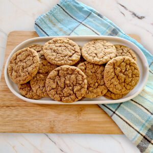 gluten free molasses crinkle cookies on a white oval dish with a blue plaid towel and wooden cutting board under