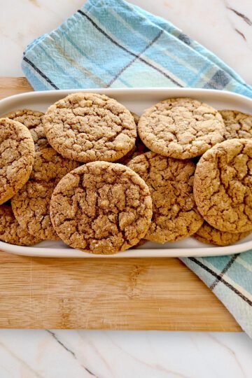 gluten free molasses crinkle cookies on a white oval dish with a blue plaid towel and wooden cutting board under