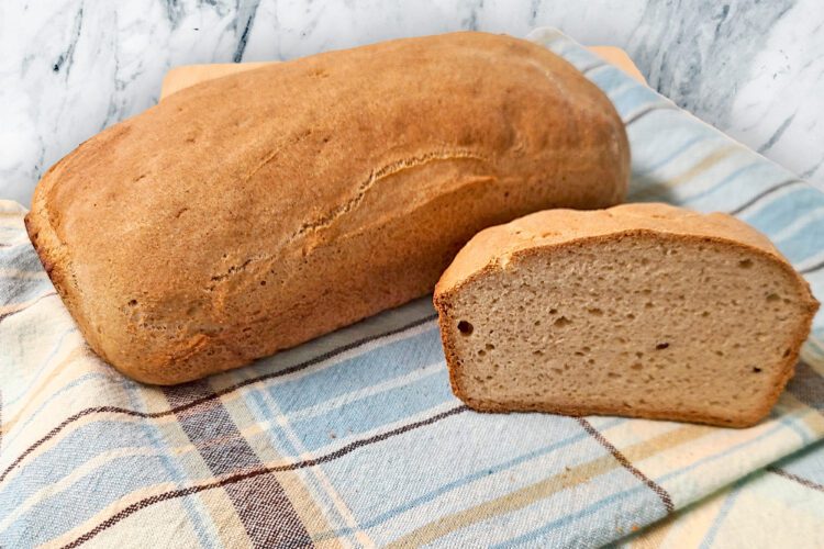 Emma's gluten free loaf bread on a plaid blue and brown tea towel on the counter