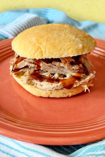 Smoked Shredded Pork served on a gluten free bun with BBQ sauce on a salmon colored plate