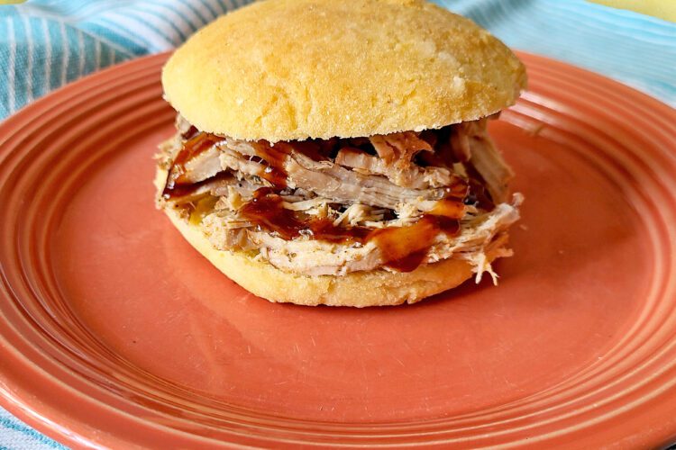 Smoked Shredded Pork served on a gluten free bun with BBQ sauce on a salmon colored plate