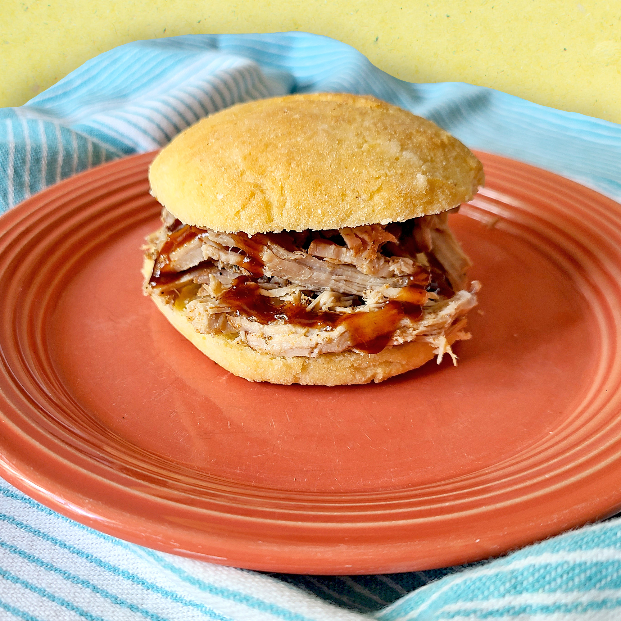 Smoked Shredded Pork served on a gluten free bun with BBQ sauce on a salmon colored plate