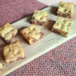 Gluten free chocolate chip cookie bars sitting on an oval wooden cutting board with a red table runner underneath