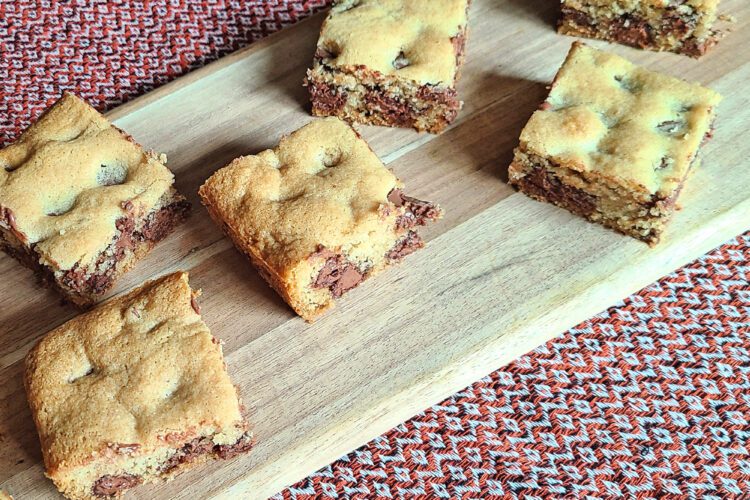 Gluten free chocolate chip cookie bars sitting on an oval wooden cutting board with a red table runner underneath