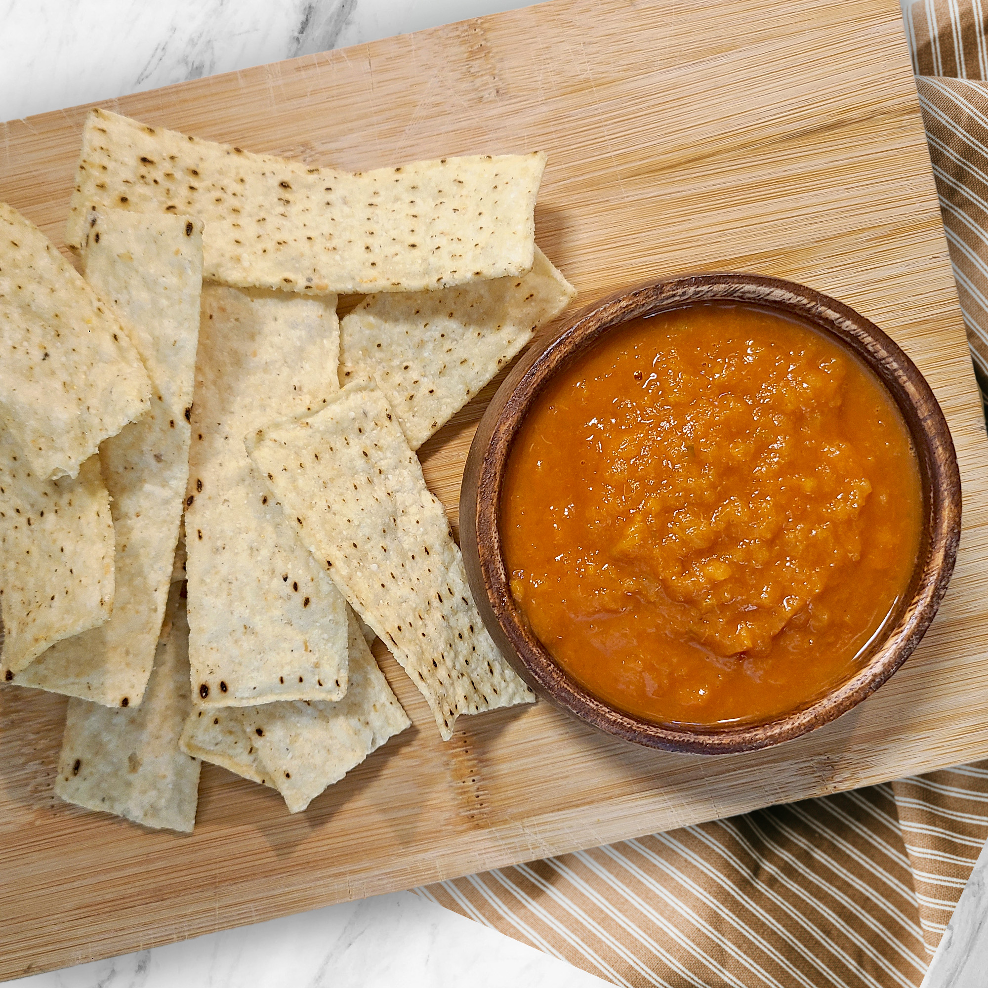 a small bowl of fresh peach & pepper salsa on a wooden cutting board with tortilla chips around it