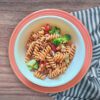 Fresh Lentil Pasta Salad in a white bowl on a pink plate with a striped tea towel underneath