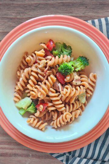 Fresh Lentil Pasta Salad in a white bowl on a pink plate with a striped tea towel underneath