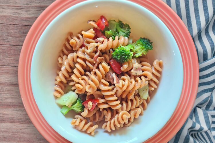 Fresh Lentil Pasta Salad in a white bowl on a pink plate with a striped tea towel underneath